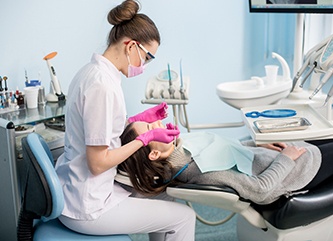 Woman in dental chair with hygienist in pink gloves about to clean her teeth