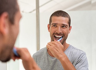 Man smiling while brushing his teeth in bathroom
