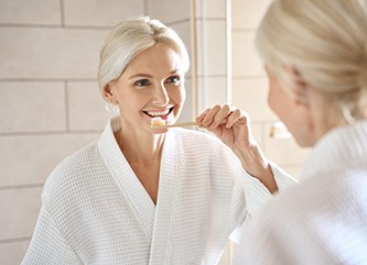 A middle-aged woman brushing her teeth in front of a bathroom mirror