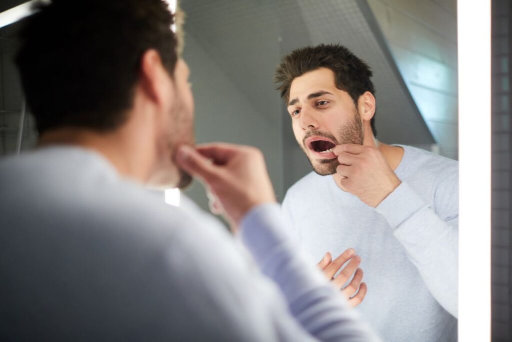 A man looking at his tooth in the mirror